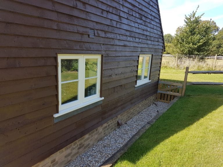White timber windows on a dark timber clad building facing a lawn