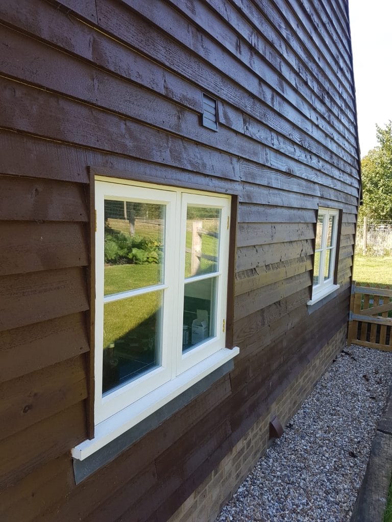 White timber casement window in dark weatherboarding beside a gravel path