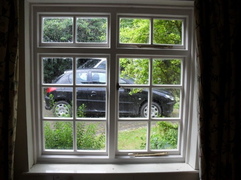 White timber casement windows framing a driveway and planting