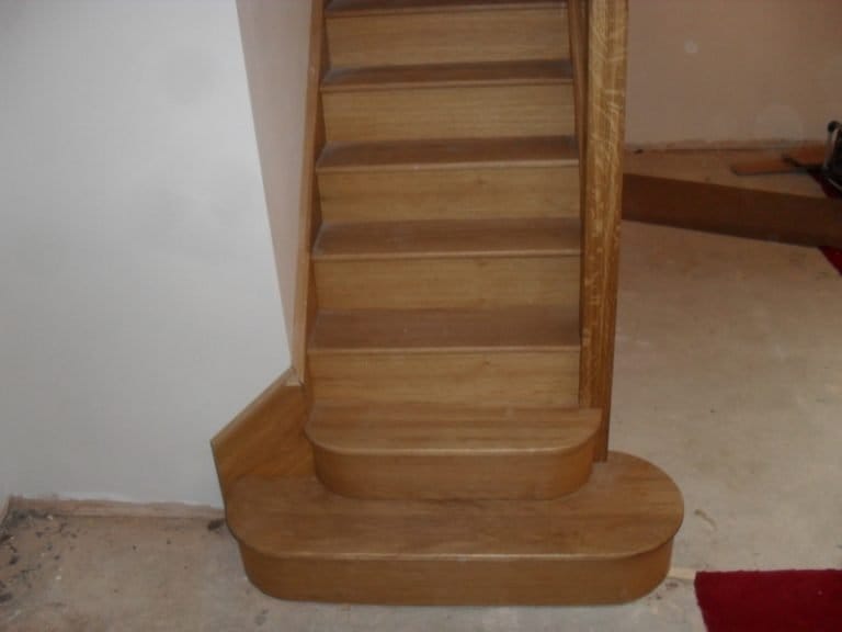 Timber staircase with curved bottom steps in a white hallway
