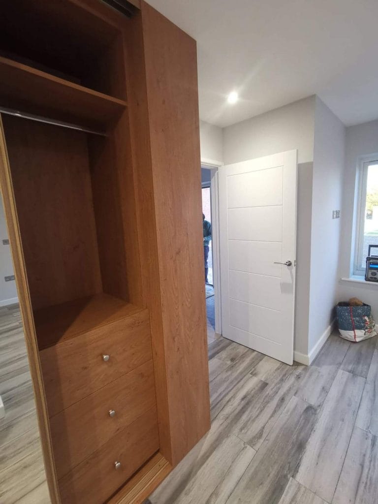 Timber fitted wardrobe with open shelving beside a white door