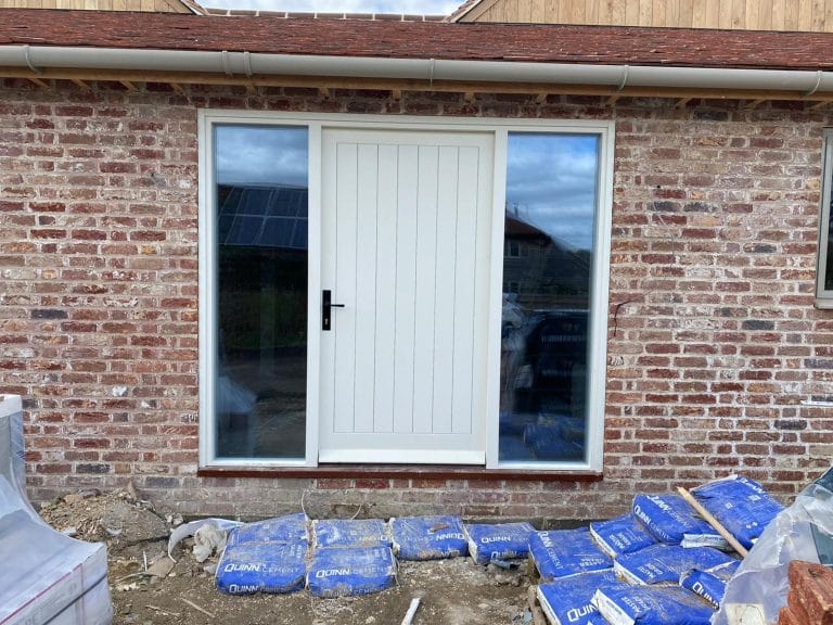 Cream boarded front door with glazed side panels on a brick cottage