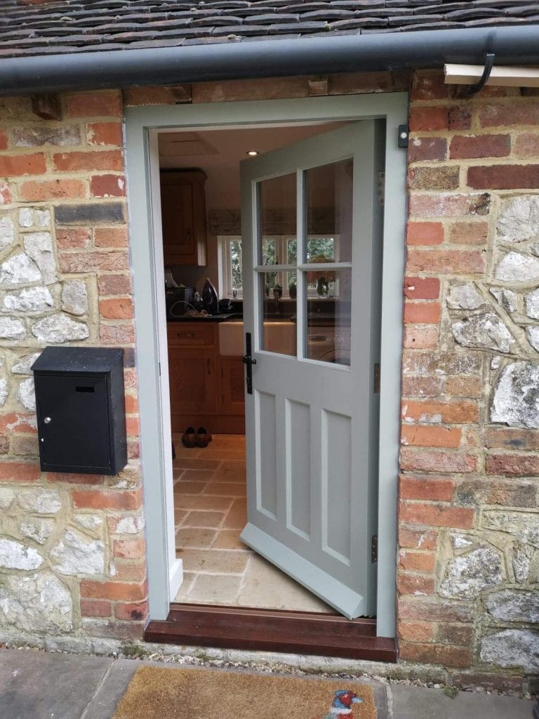 Grey painted glazed door in a flint wall next to a wall mounted post box