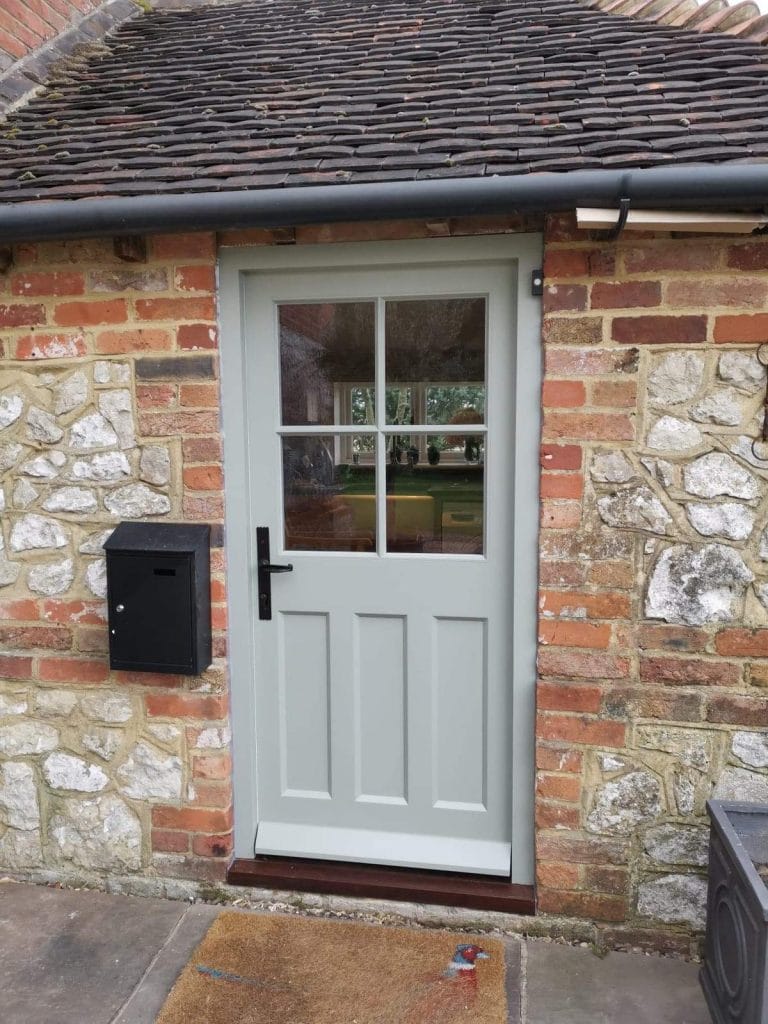 Grey painted half glazed door in a flint and brick wall beside a black post box