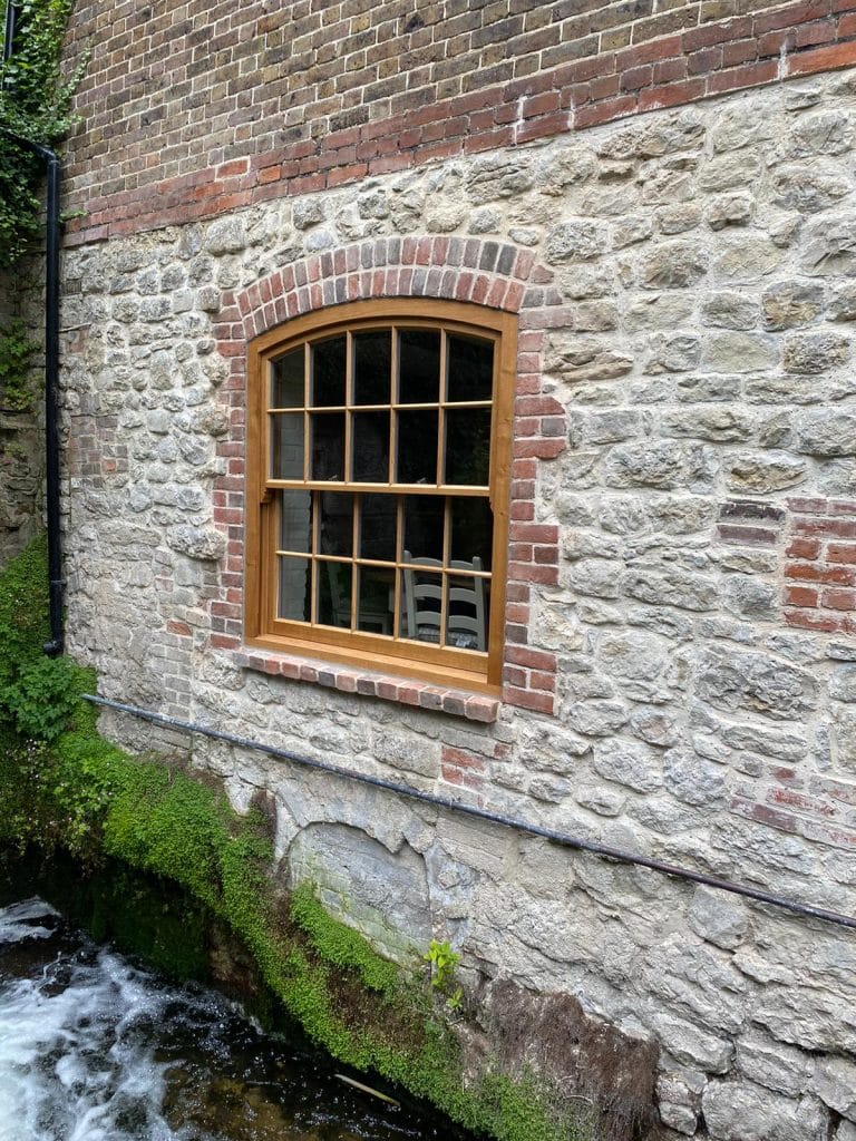 Arched natural timber sash window on a flint and brick building