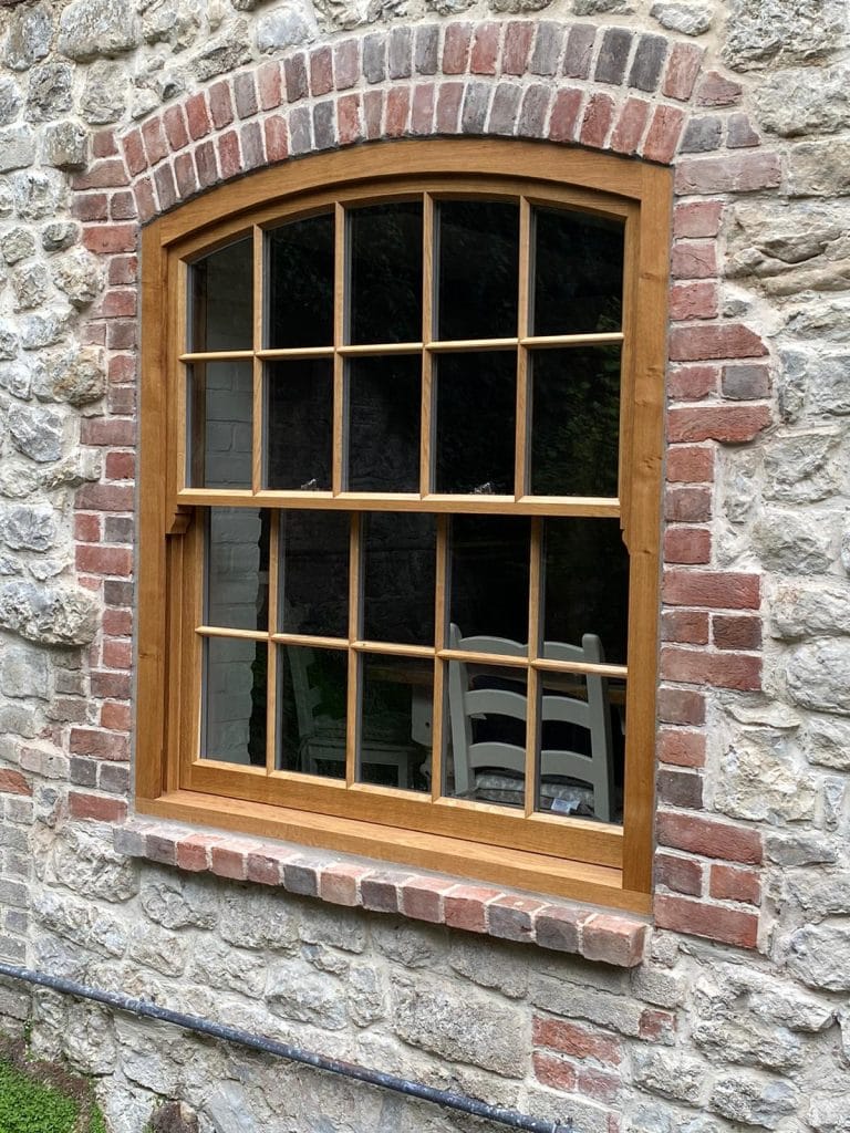 Close up of an arched timber sash window set in flint and brick