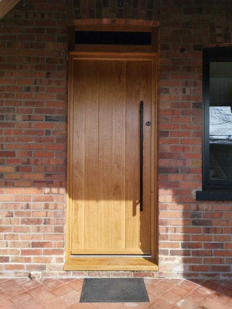 Natural timber front door with a full height black pull handle in brickwork