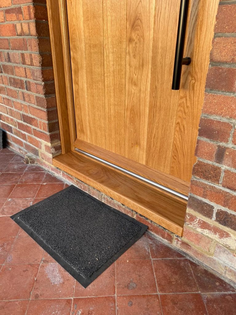 Detail of a natural timber door frame meeting red brickwork at the threshold