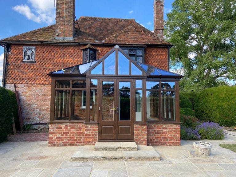 Timber conservatory with a pitched glass roof on a brick farmhouse