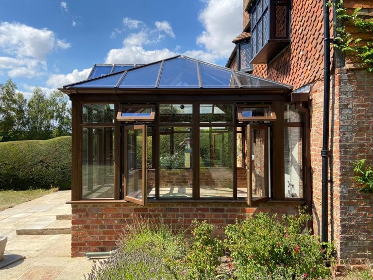 Stained timber conservatory with hipped glass roof on a brick base