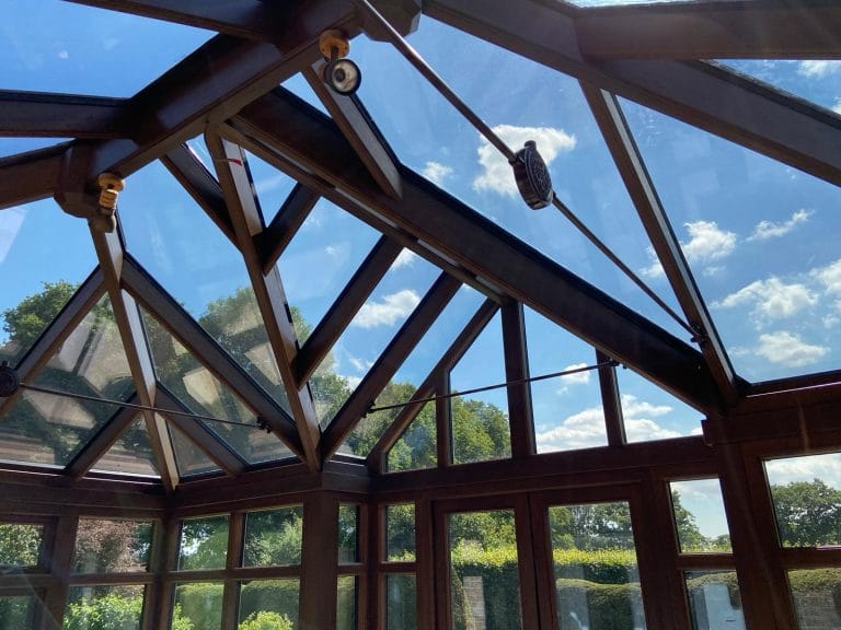 Stained timber conservatory roof with glazing bars against a blue sky