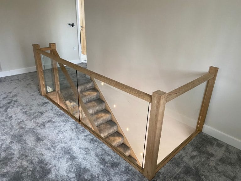 Carpeted staircase with timber handrail and glass panels