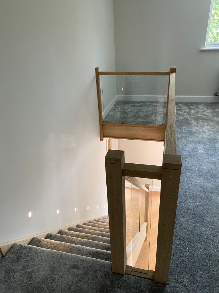 Timber newel post and glass balustrade at a carpeted landing