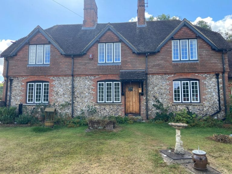 Flint cottage with white timber windows and a natural wood front door