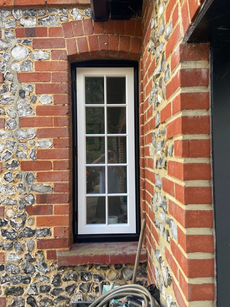 Narrow white timber sash window in a flint and brick wall