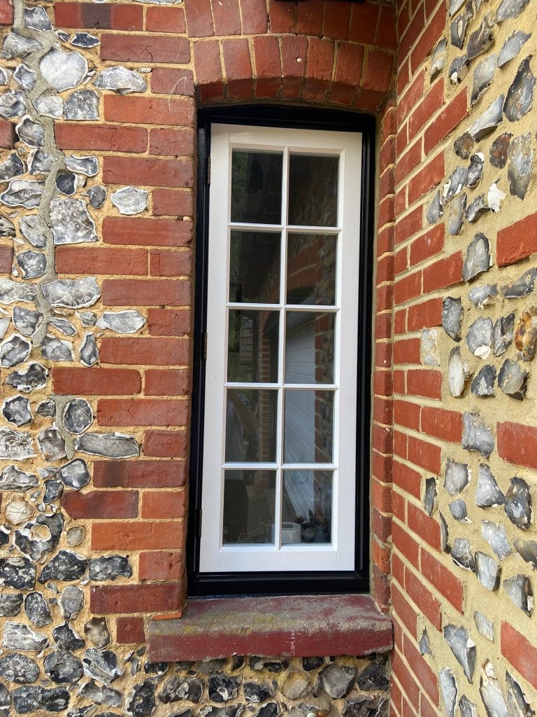 White timber sash window set between flint and brick reveals