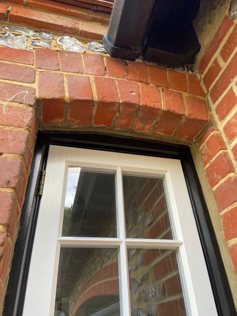 White timber casement window under a red brick arch