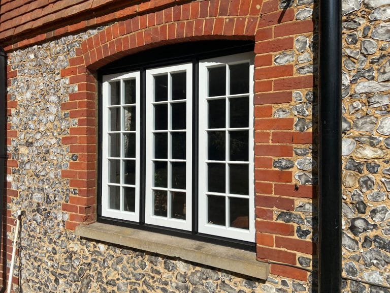 Black and white timber casement windows in a flint and brick wall